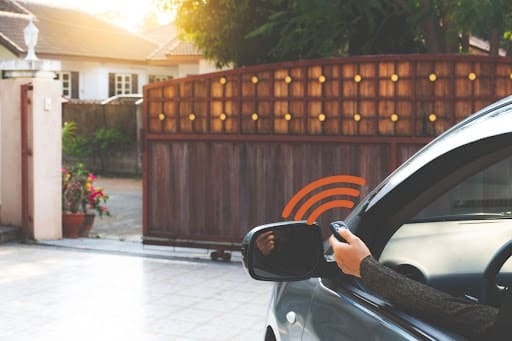 A person in a car using a button to open an automatic gate outside a home.